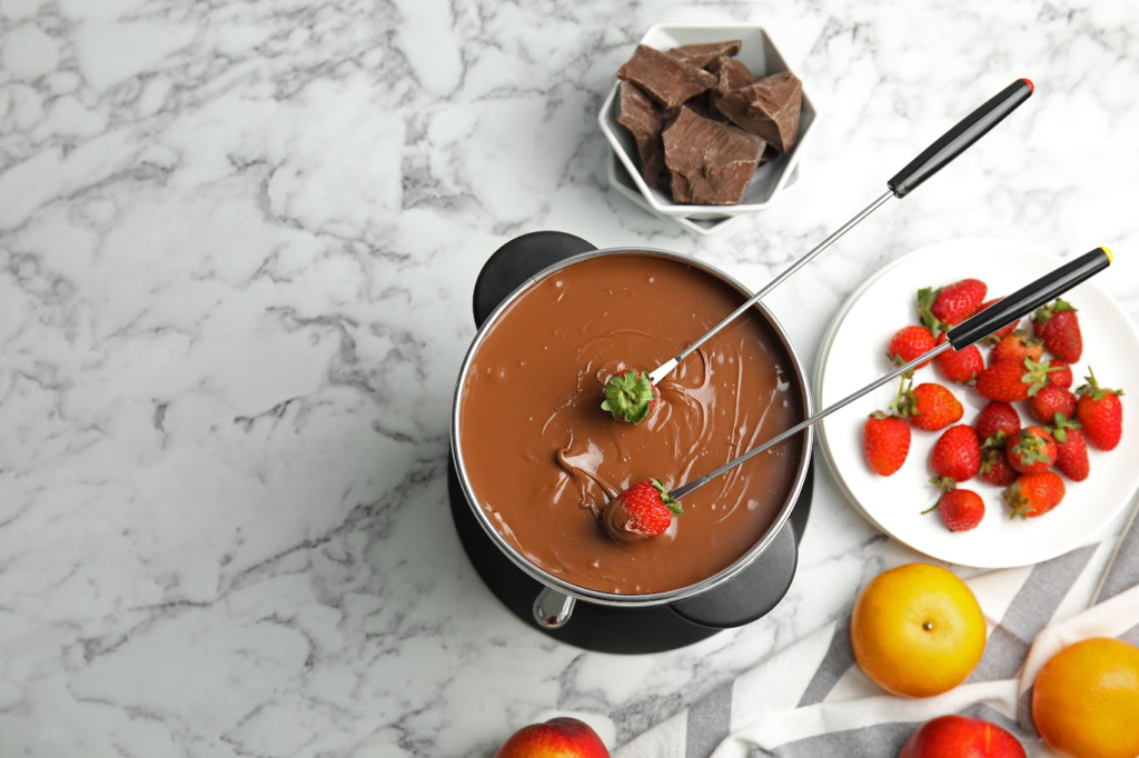 A imagem ilustra uma mesa com frutas para fondue, com muitos morangos e chocolate no rechaud.