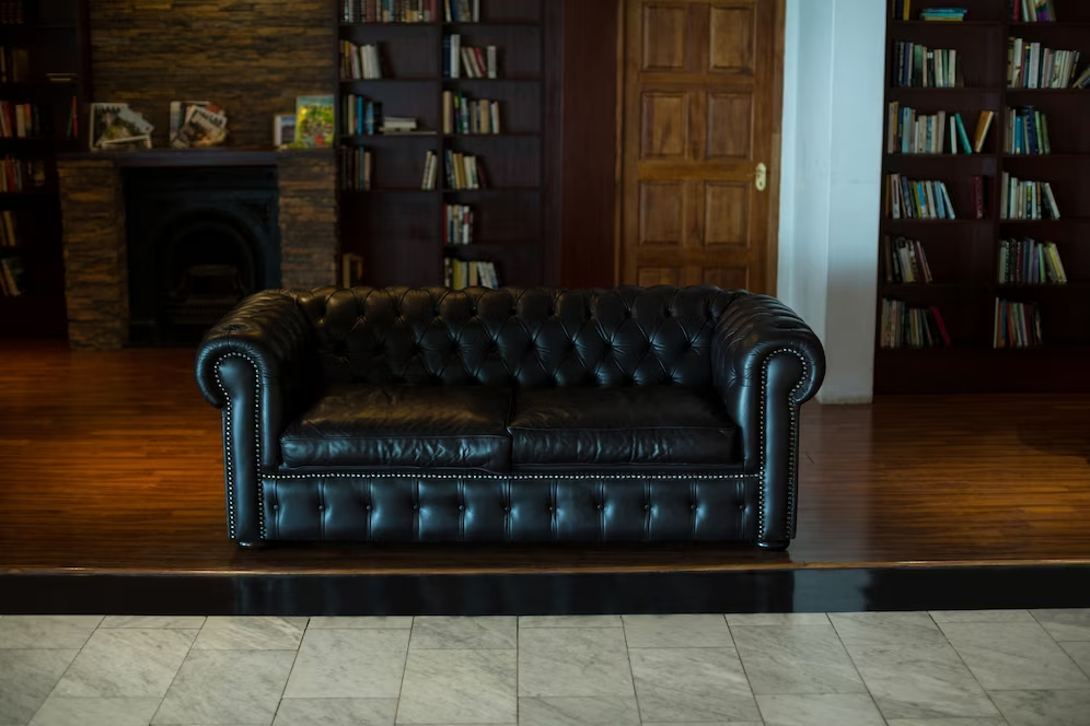 A imagem ilustra um sofá de couro preto em uma sala com móveis de madeira, compondo o look de inverno da casa.