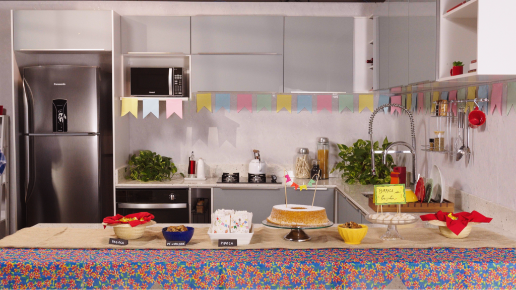 A imagem ilustra uma cozinha completa madesa com uma bancada repleta de tudo o que tem na festa junina em comidas.