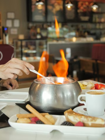 A imagem ilustra um rechaud e frutas para fondue com chamas acesas sobre uma mesa.