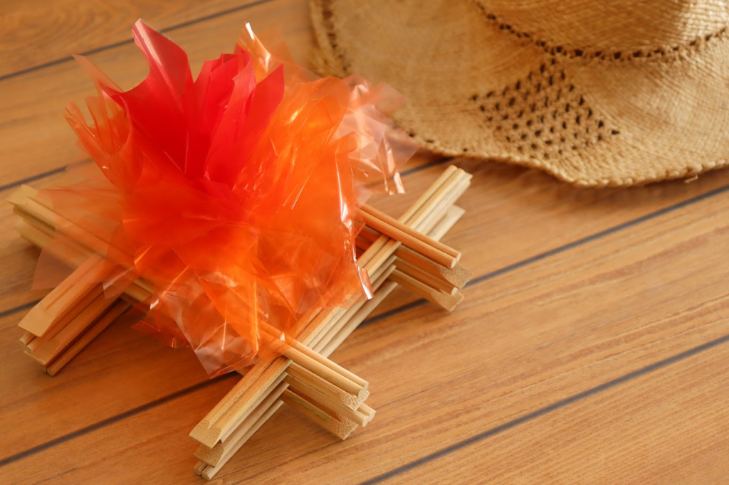 A imagem ilustra uma mini fogueira feita com papel celofane e palitos de madeira, simbolizando o que tem na festa junina de decoração.
