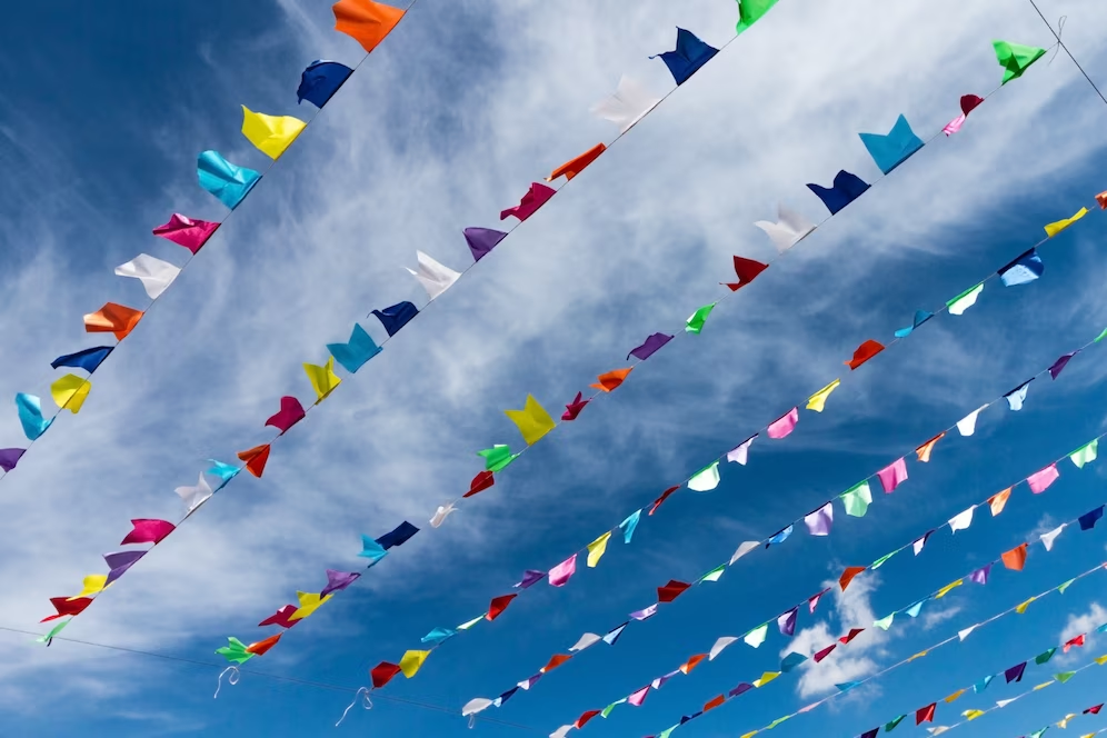 A imagem ilustra um céu azul e sobre ele muitas bandeirinhas de festa junina.