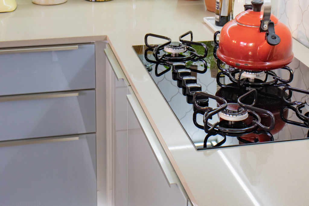 : O balcão de uma cozinha Madesa está com um cooktop acoplado à sua superfície. Sobre o cooktop está um bule vermelho.