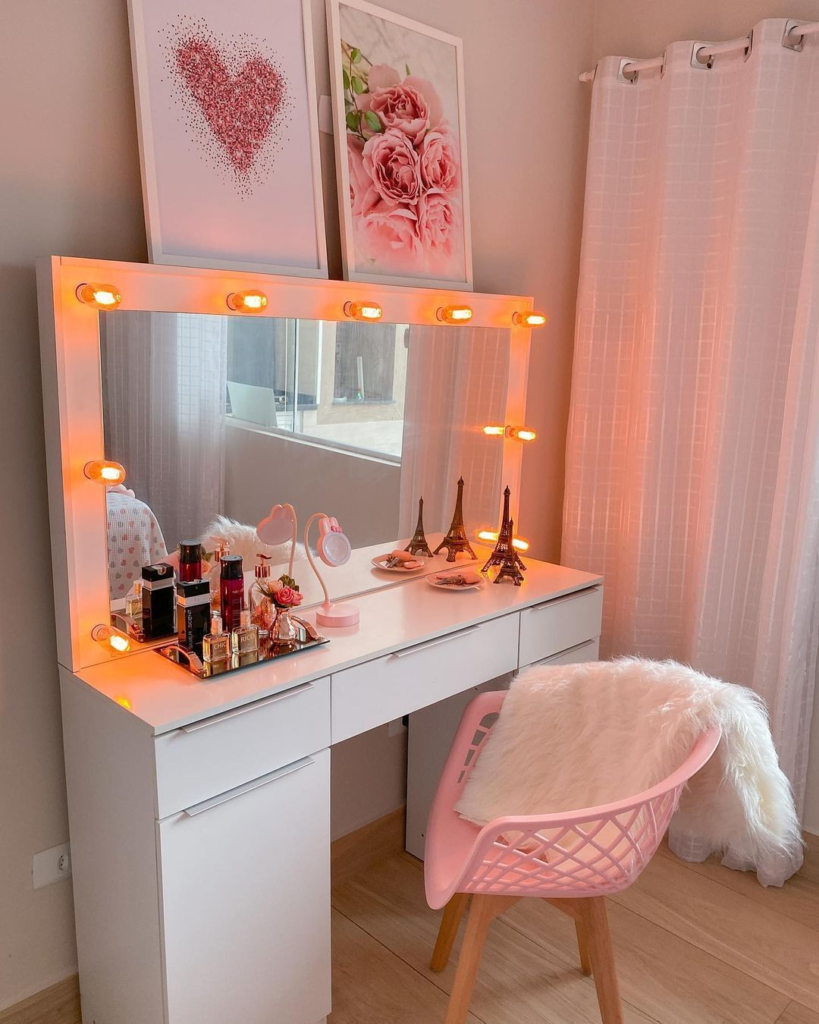A imagem ilustra cores que combinam com rosa através de quarto com penteadeira e quadros de parede brancos. Também há uma cadeira rosa  claro com uma manta de pelúcia branca sobre ela.
