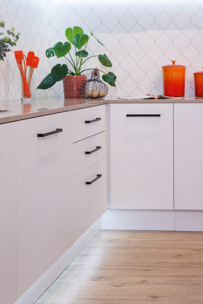 A imagem ilustra o canto de uma cozinha planejada em L branca, composto por plantas e utensílios de cozinha.