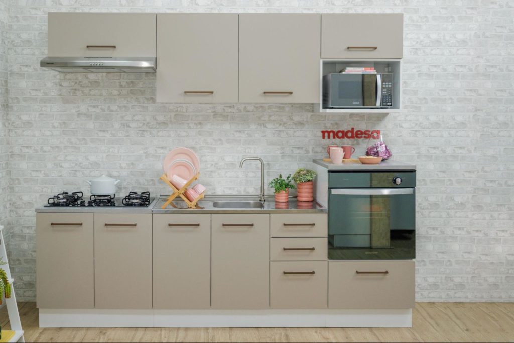 A imagem ilustra uma cozinha planejada na cor crema, uma das cores que combinam com o rosa dos pratos e vasos de plantas que estão sobre a sua bancada.