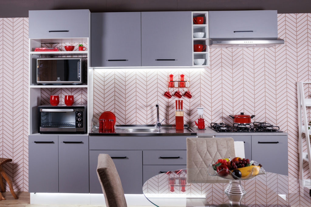A imagem ilustra uma cozinha gourmet pequena na cor azul com objetos decorativos na cor vermelha.