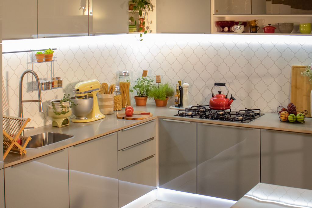 A imagem ilustra uma cozinha planejada Madesa na cor cinza, em cima de sua bancada há muitos eletrodomésticos e itens de cozinha.