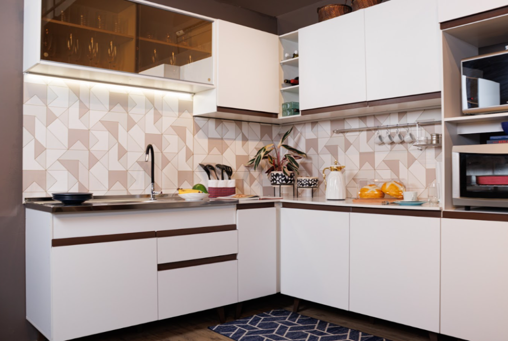 A imagem ilustra um dos modelos de cozinhas Madesa, a cozinha Reims, em formato de L na cor branca com acabamento em madeira.