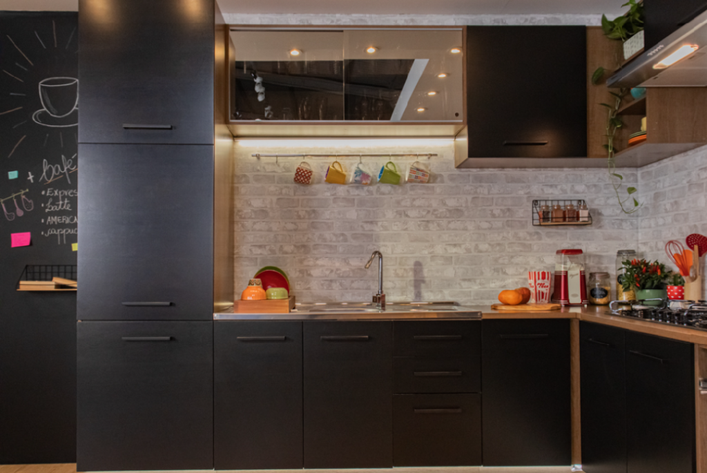 A imagem ilustra um dos modelos de cozinhas da Madesa, na cor preto fosco com utensílios de cozinha em cima da bancada. 