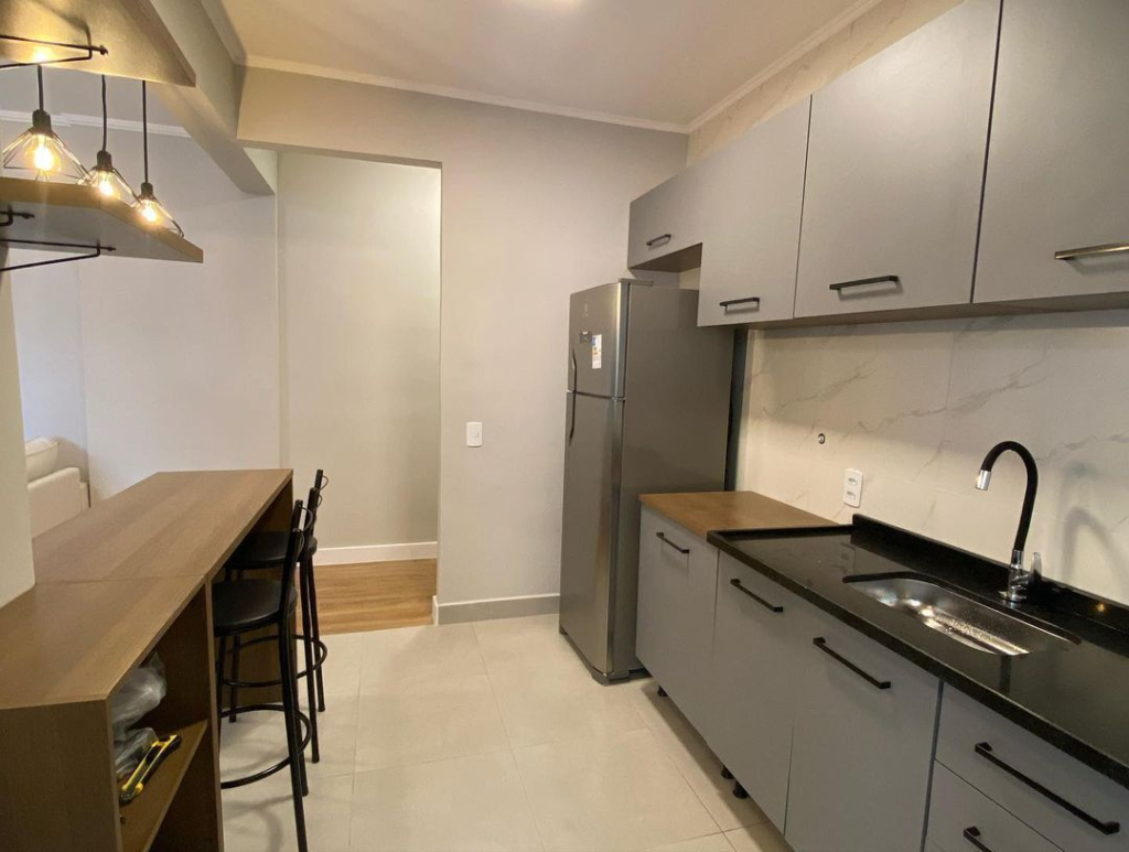 A imagem ilustra uma cozinha planejada americana com armários planejados na cor cinza e um balcão de madeira que divide a sala e a cozinha.