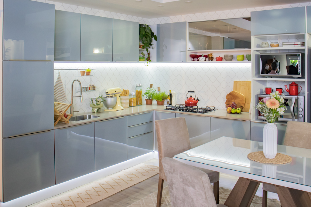 A imagem ilustra uma cozinha planejada Lux nas cores branco e cinza, com uma mesa de jantar decorada.