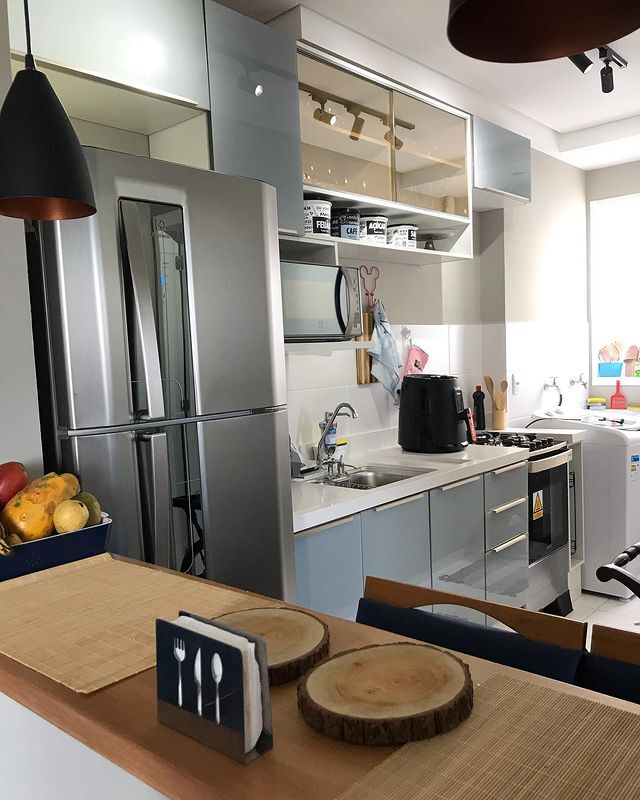 A imagem ilustra uma cozinha americana planejada de apartamento na cor cinza. Na divisão dos cômodos há um balcão de madeira.
