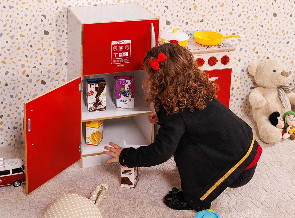 A imagem ilustra uma menina, brincando com a geladeira infantil de madeira Madesa.