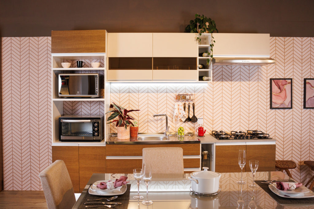 Cozinha decorada da linha Glamy Rustic, nas cores branco e crema. À frente dos módulos, há uma mesa de jantar posta.