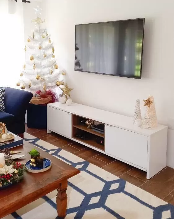 Sala de estar com decorações nas cores branco e azul. Ao lado, uma árvore de Natal branca com bolas douradas.