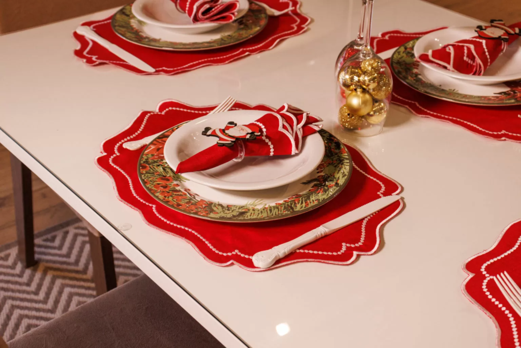 Mesa posta de Natal, decorada com toalha de mesa vermelha e guardanapos dobrados com estampa de Papai Noel.