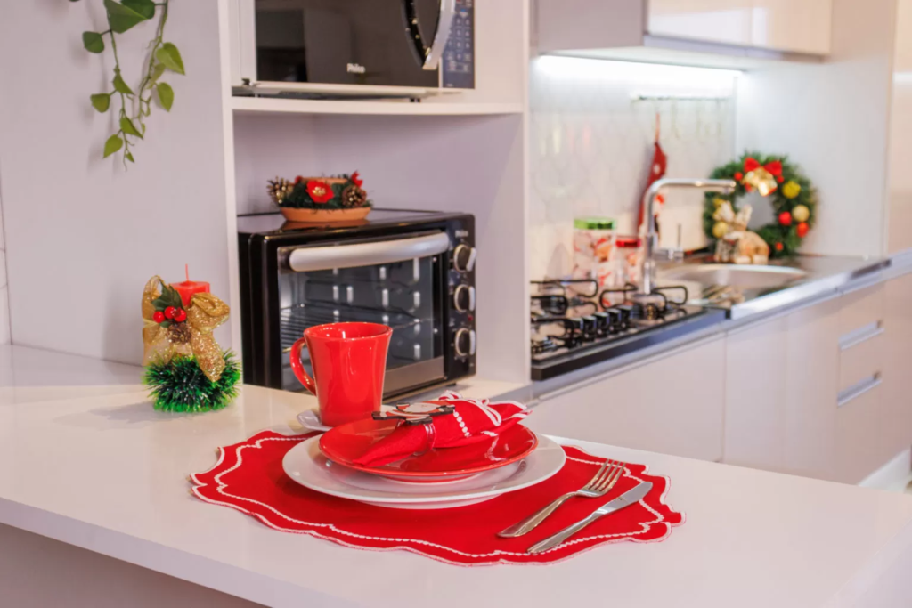 Bancada de cozinha decorada com toalha de mesa, prato, caneca e guardanapos vermelhos para trazer o clima natalino.