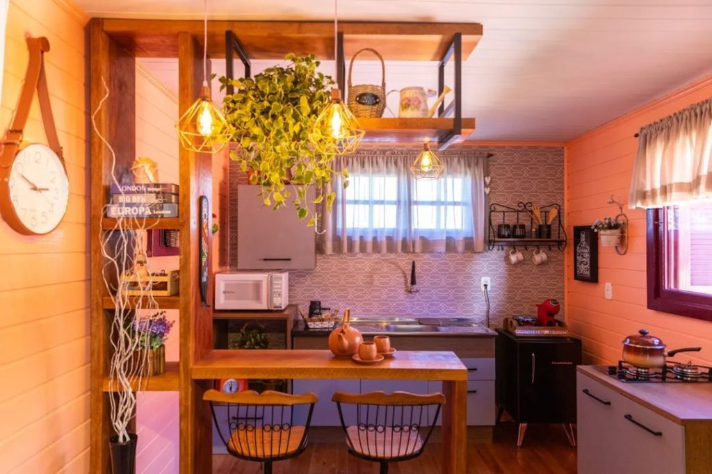Cozinha Madesa, nas cores rustic e branco, com uma bancada e estante amadeirados e decorado com muitas plantas e cerâmicas.