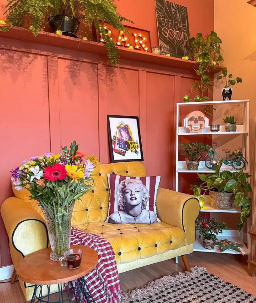 Sala de estar com sofá amarelo e uma almofada estampada, estante escada Madesa com muitas plantas e muitos quadros estampados.
