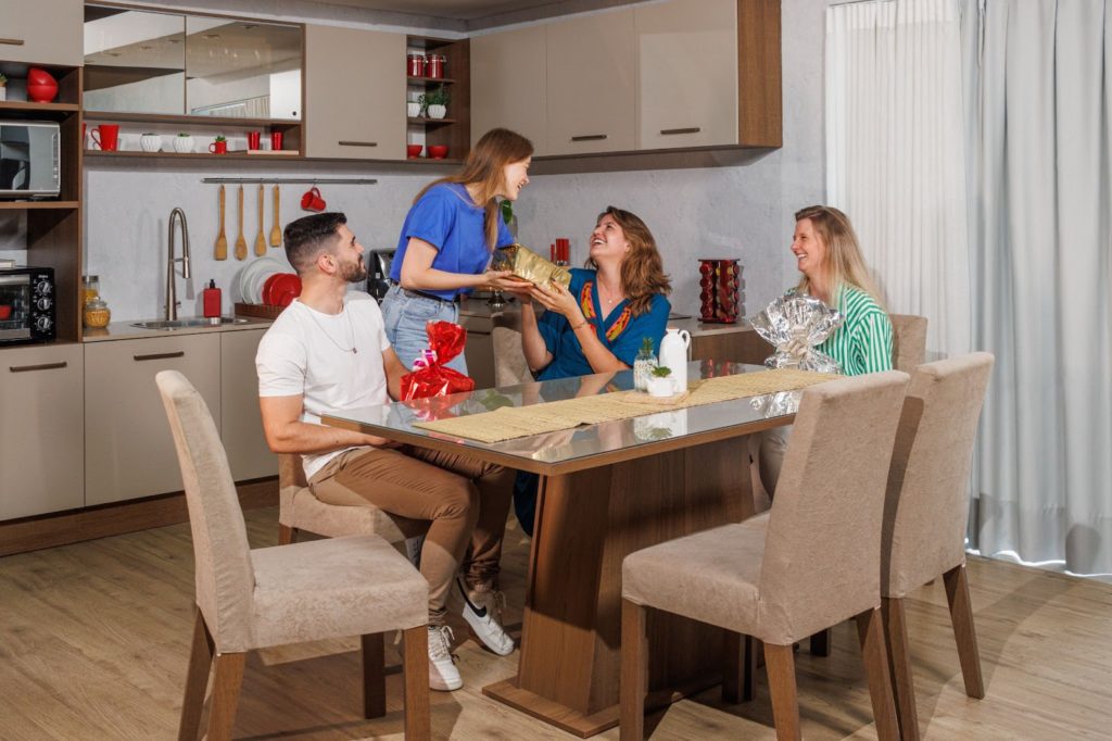 Família reunida, sentada à mesa de jantar enquanto compartilham presentes, sorrindo.