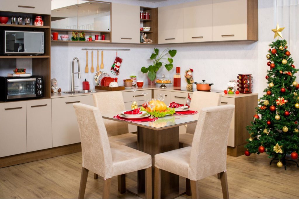 Cozinha completa Madesa, decorada com utensílios natalinos e eletrodomésticos. Ao centro, uma mesa de jantar posta para o Natal, e uma àrvore à direita.