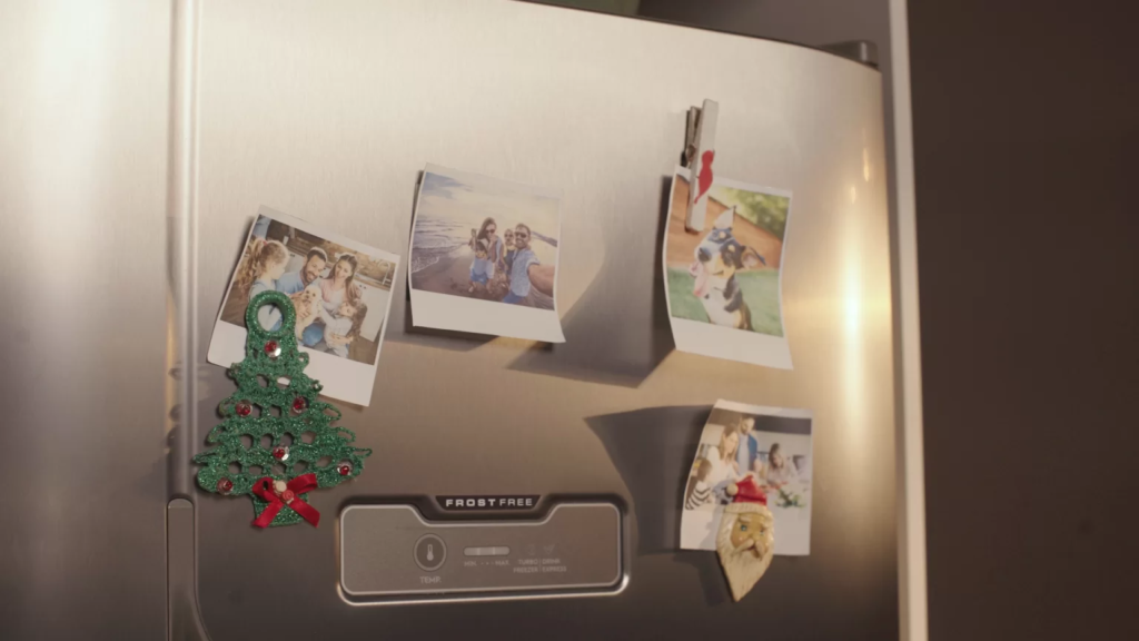 Geladeira decorada com imãs temáticos de Natal, prendendo fotos de família no eletrodoméstico.