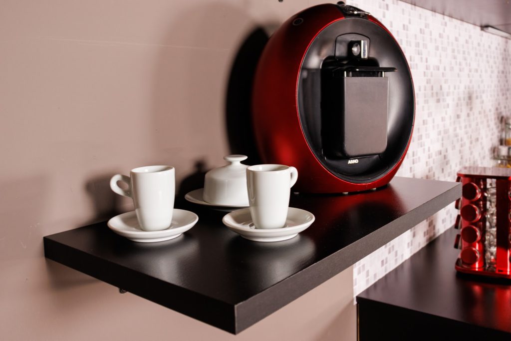 Prateleira Madesa, na cor preta, decorada com xícaras e uma cafeteira vermelha.