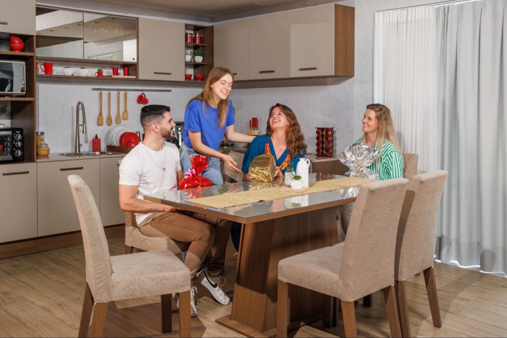 Família reunida em volta da mesa de jantar Madesa, sorrindo enquanto trocam presentes. Ao fundo, uma cozinha Madesa decorada.