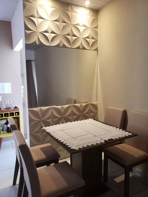 Mesa de jantar quadrada Madesa, decorada com uma toalha bordada. Ao lado, um espelho com parede texturizada e iluminação amarela no teto.