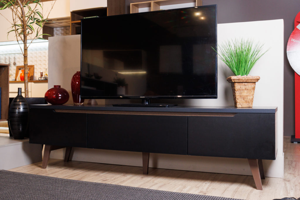 Rack Reims Madesa, na cor preta, decorado com uma TV, vasos de vidro e uma planta.
