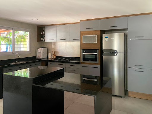 Cozinha ampla com armários Madesa na cor cinza, eletrodomésticos em inox e bancadas na cor preta.
