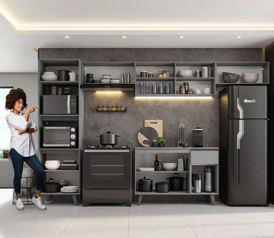 Mulher do lado esquerdo apontando para a cozinha preta e cinza Madesa, composta por móveis e eletrodomésticos nas duas cores.