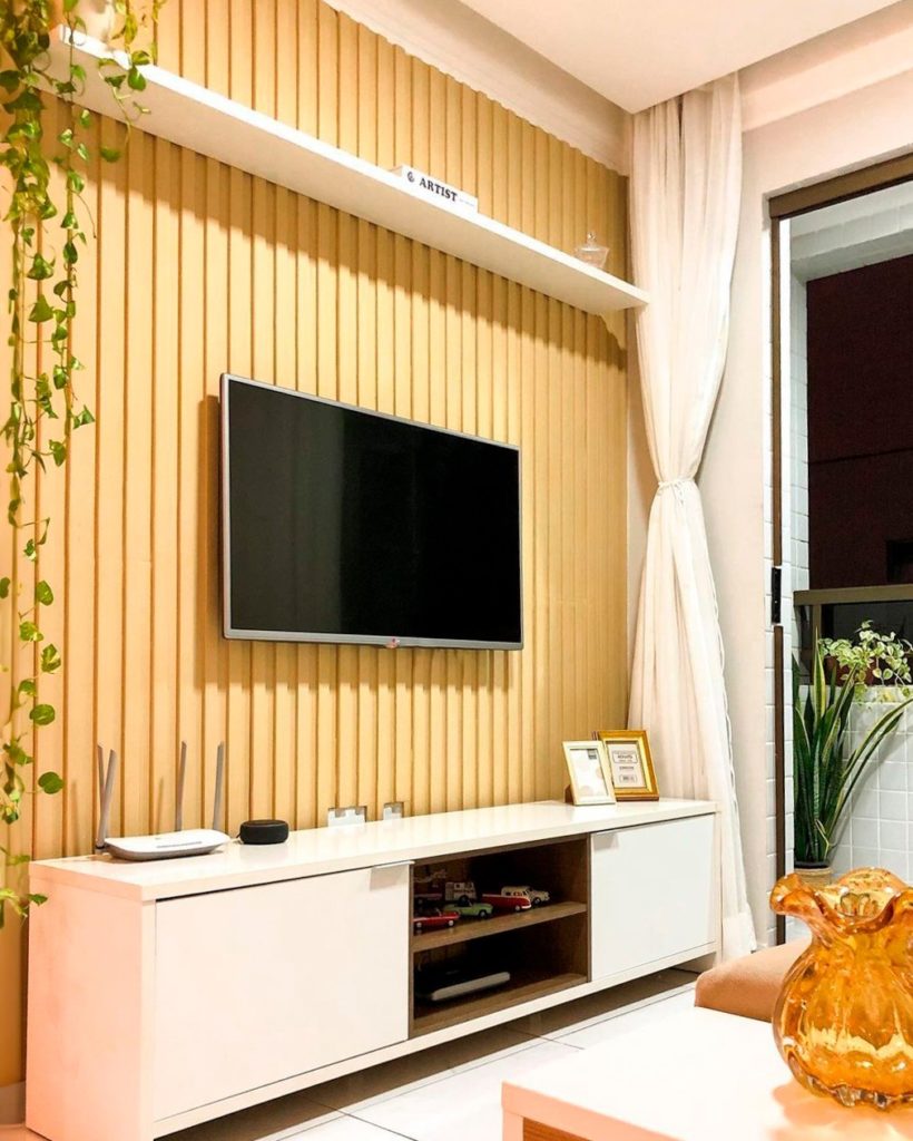 Sala de estar com uma parede ripada em madeira na cor clara, rack branco Madesa com porta-retratos e objetos decorativos diversos. 