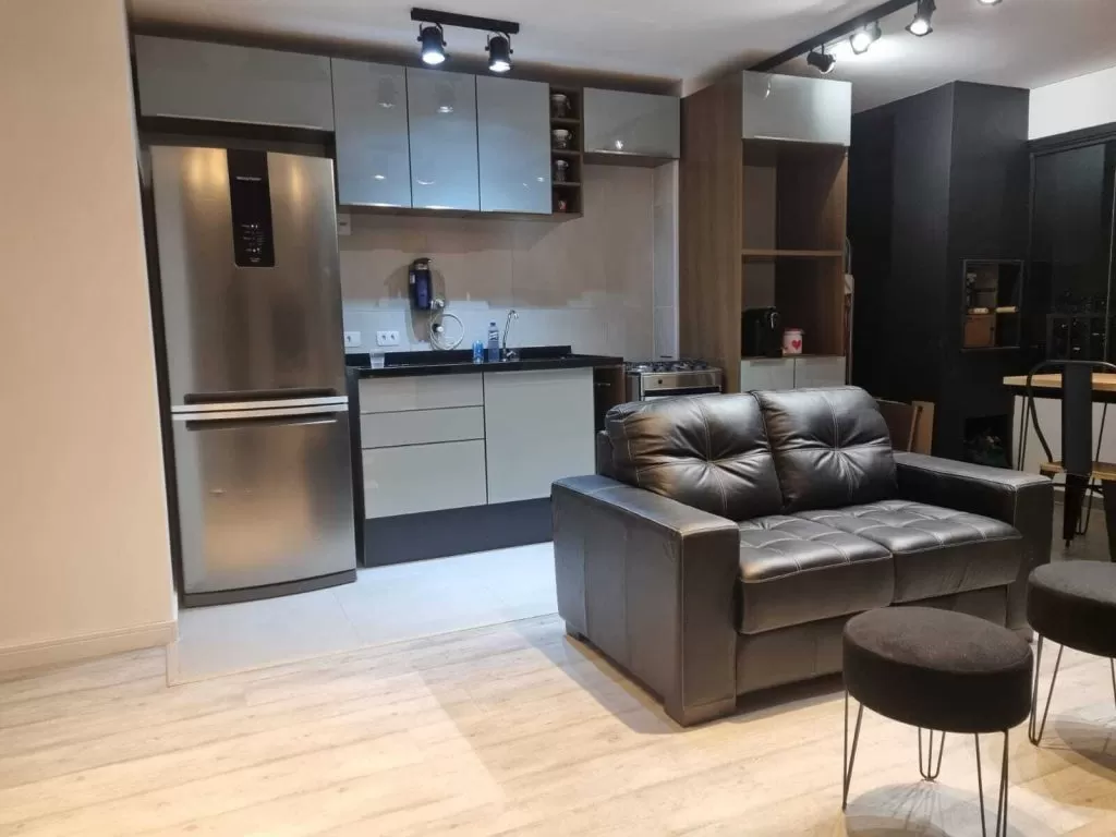 Cozinha Madesa nas cores cinza e preto, integrada com uma sala de estar com sofás e bancos pretos.