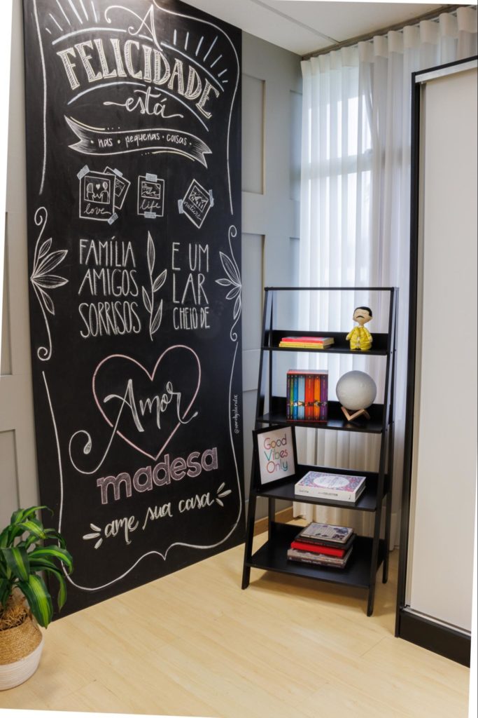 Estante escada Madesa, na cor preta, decorada com livros e objetos decorativos. À esquerda, um quadro com frases motivacionais e o slogan “Madesa, ame sua casa”.