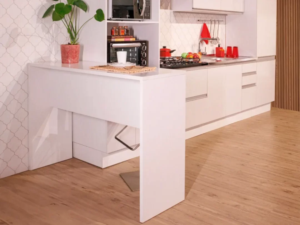 Bancada Madesa, na cor branca. Ao fundo, cozinha Madesa também branca, decorada com utensílios e eletrodomésticos.