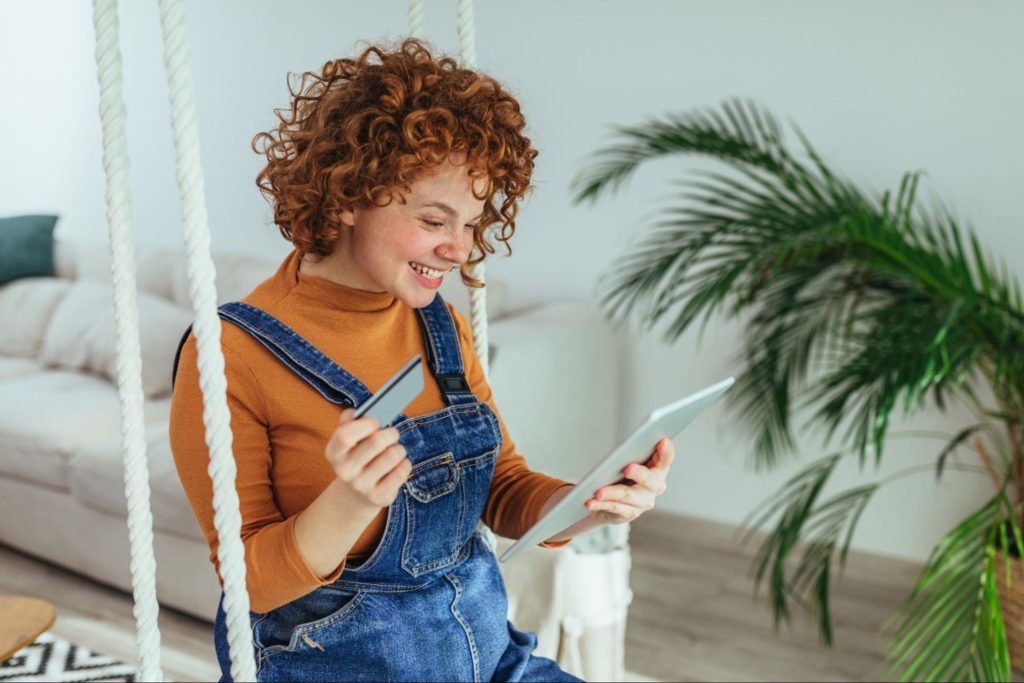 mulher ruiva fazendo compras online com o celular e um cartão de crédito nas mãos