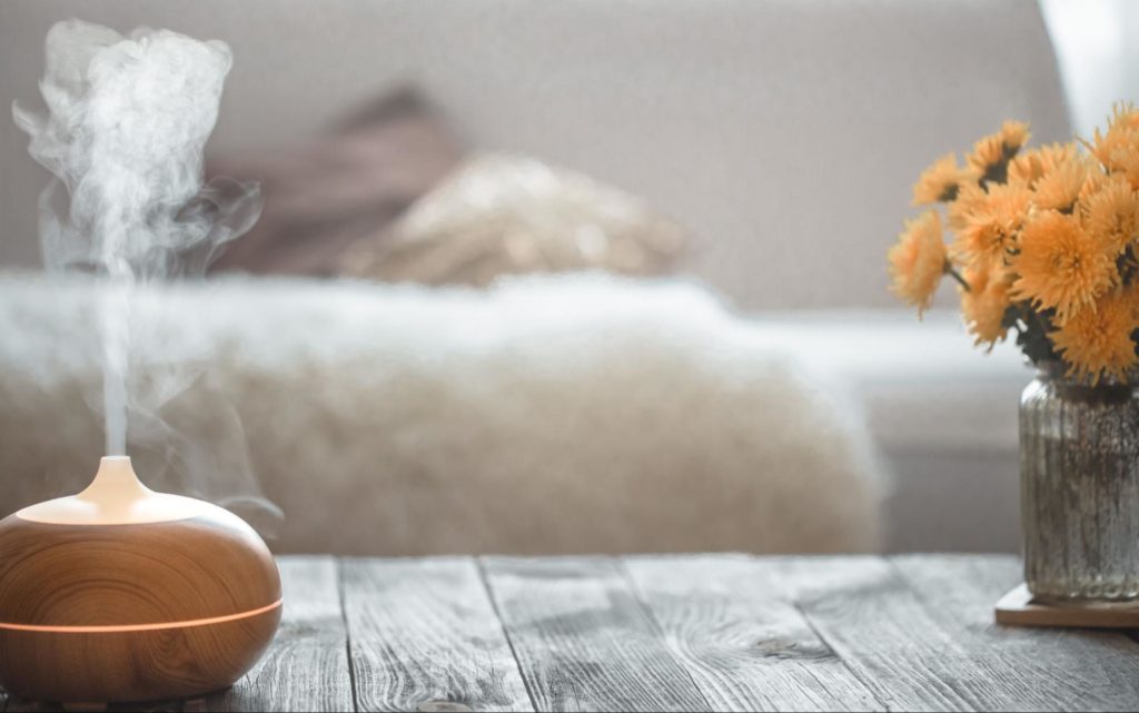  umidificador de ar disposto acima de mesa central ao lado de vaso de vidro com flores amarelas