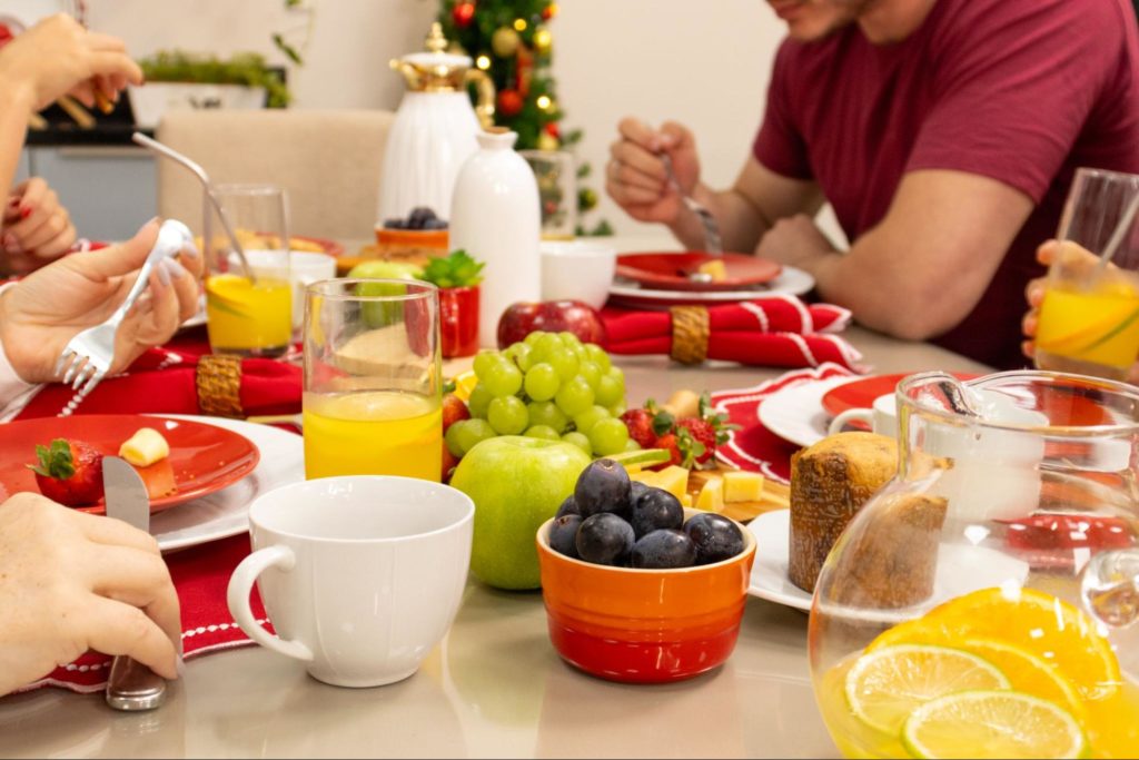 mesa de café da manhã com frutas e sucos, queijos e um panetone pequeno