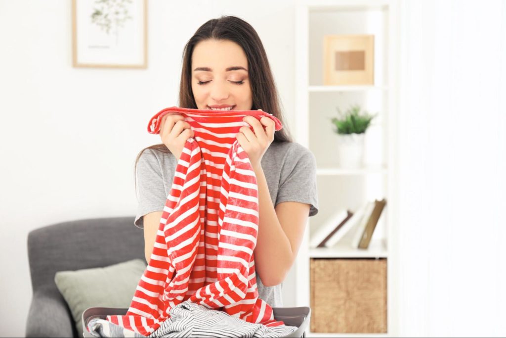 Mulher sorri enquanto segura uma camiseta listrada vermelha, dando um cheiro a ela em um ambiente aconchegante.