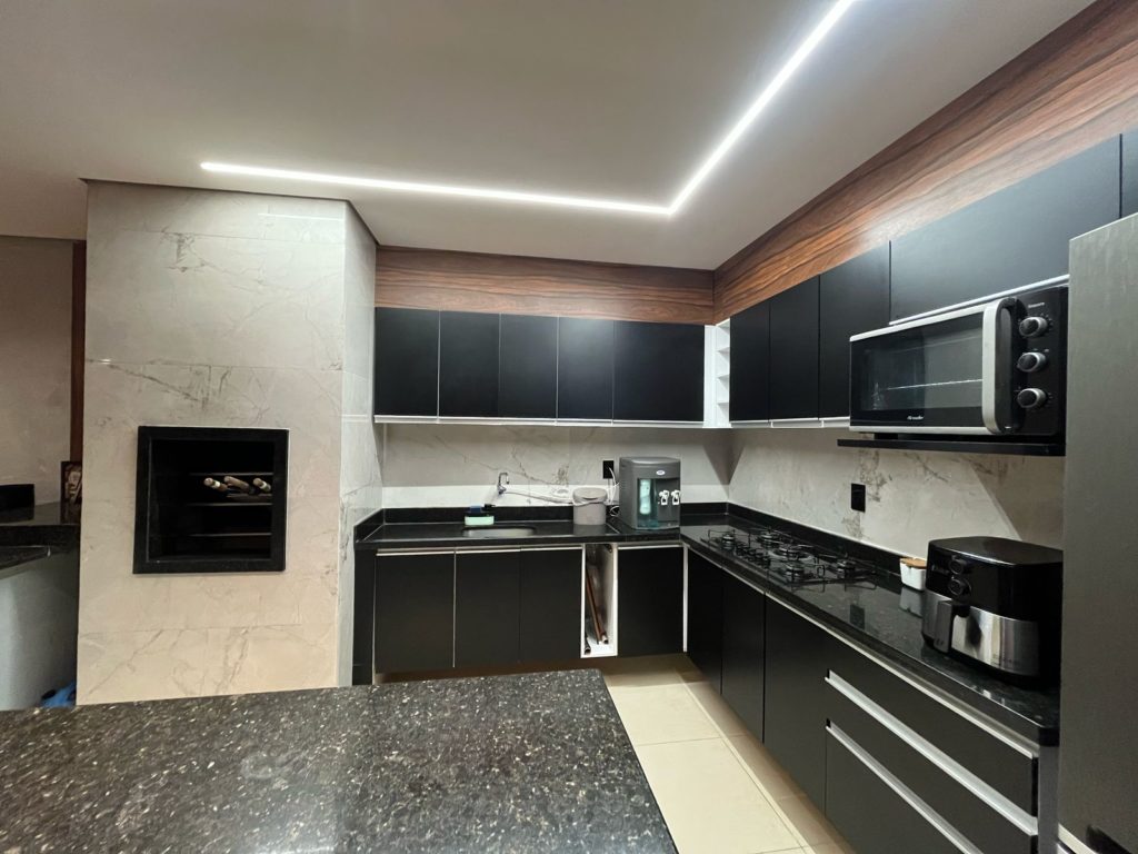Cozinha planejada com armários aéreos e gabinetes na cor preta ao lado de churrasqueira.