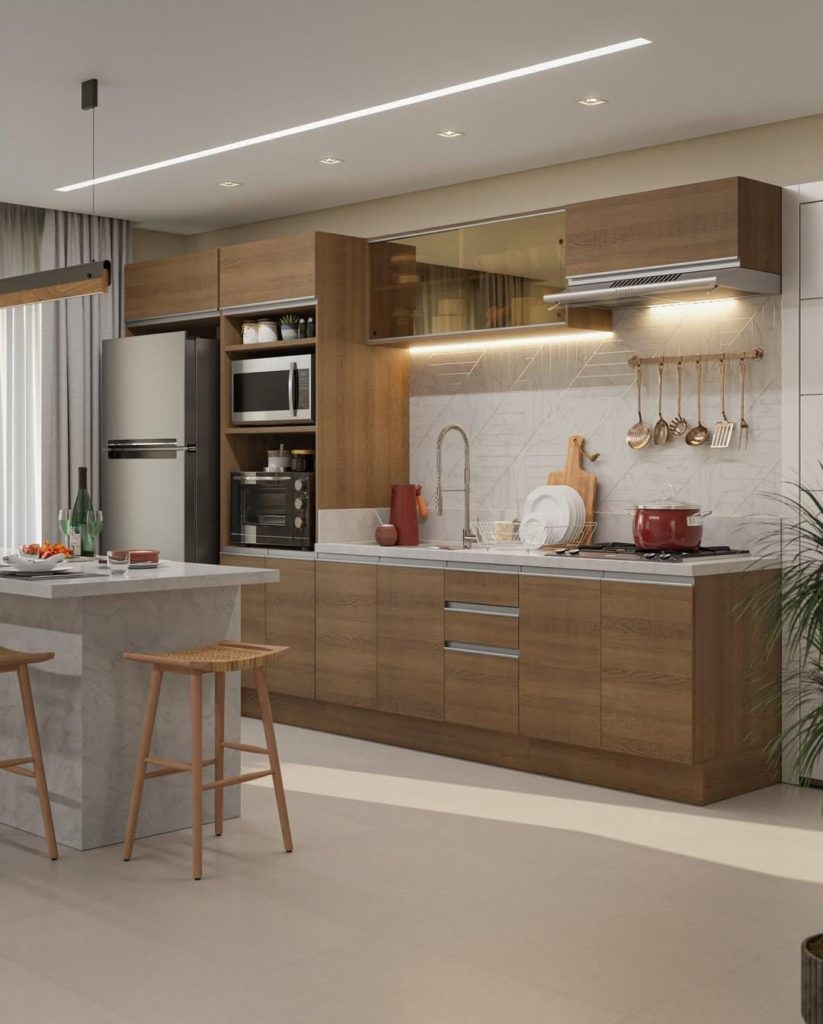 Cozinha com armários amadeirados e uma ilha com efeito mármore. Duas banquetas de madeira estão na ilha, com uma geladeira de inox e torre para fornos ao fundo.