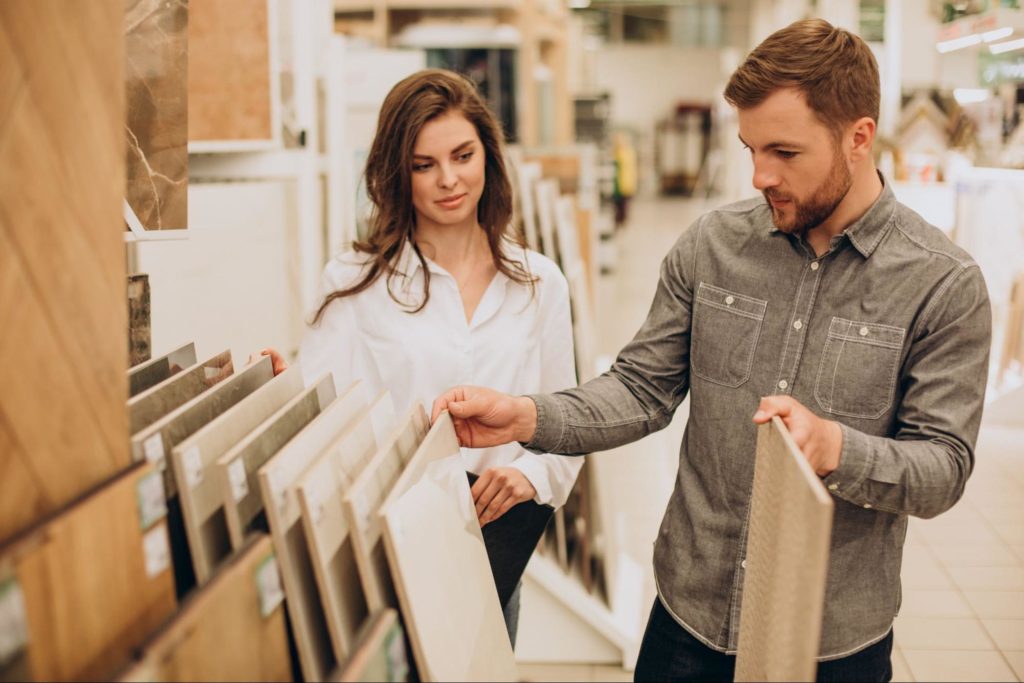 Um homem e uma mulher estão em uma loja de materiais de construção ou decoração, olhando e escolhendo amostras de pisos.