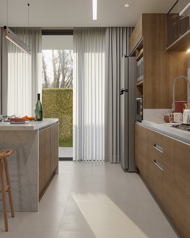 Cozinha com armários de madeira clara e branco, bancada de mármore, geladeira de inox, micro-ondas embutido, pia com torneira e cortinas brancas que cobrem uma grande janela. Há uma porta de vidro que leva ao jardim com árvores e arbustos ao fundo.