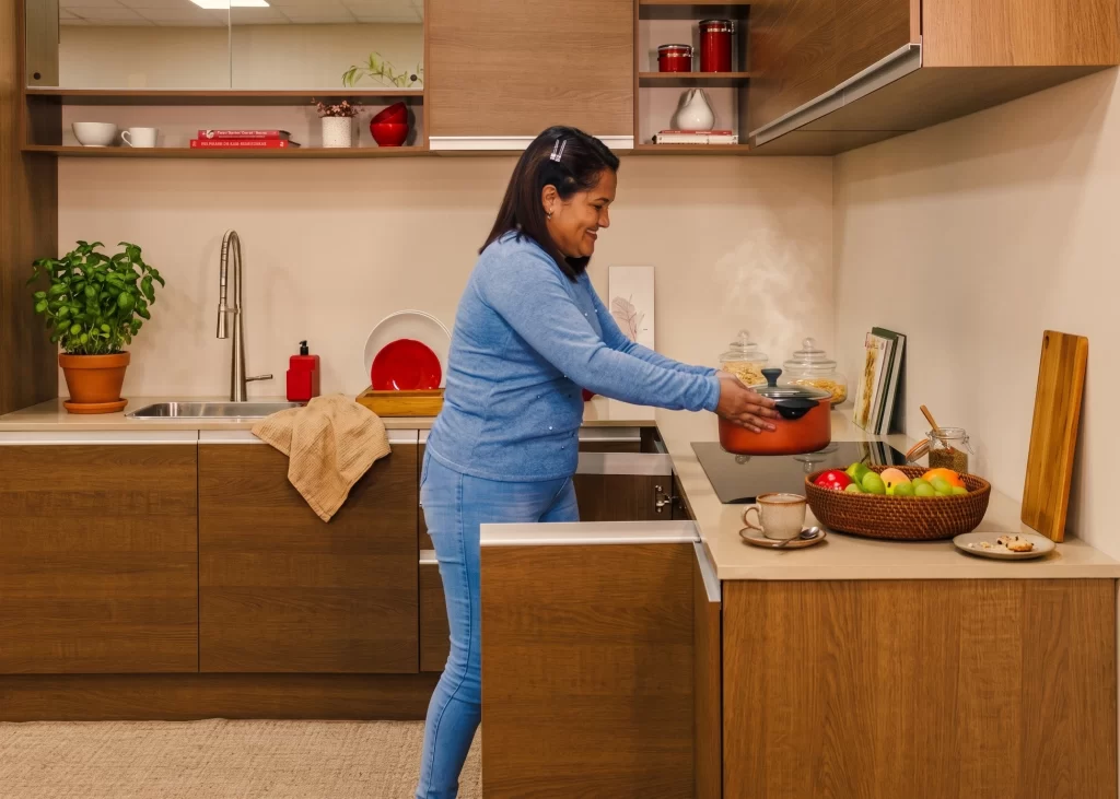 Mulher cozinhando em uma cozinha planejada amadeirada linha Glamy rustic da Madesa com cooktop e bancada clara.
