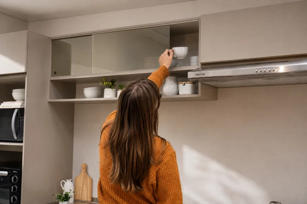 Mulher guardando uma xícara no armário aéreo de vidro de uma cozinha planejada crema linha Nice da Madesa.