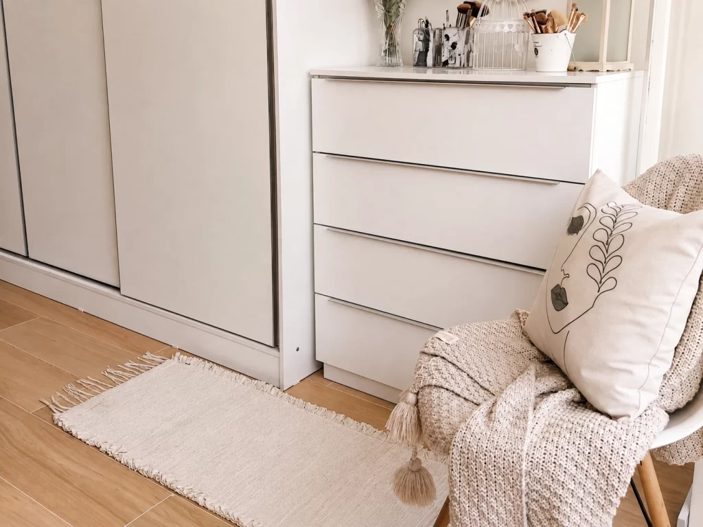 Cômoda Madesa branca da linha Laura, com quatro gavetas, ao lado do guarda-roupa no quarto.