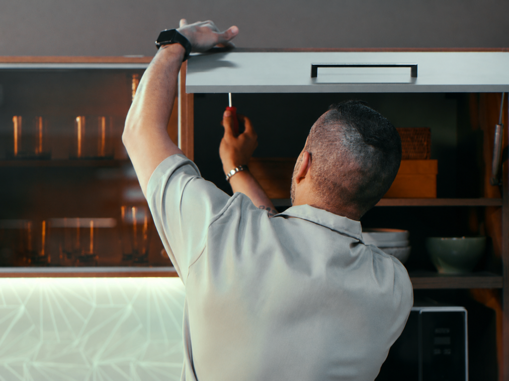 Homem ajustando com chave de fenda o acabamento de um armário escuro durante a montagem do móvel