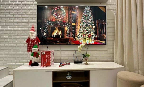 Sala de estar decorada para o Natal, com enfeites de Papai Noel, cartas de Natal e trem em miniatura em cima do rack.